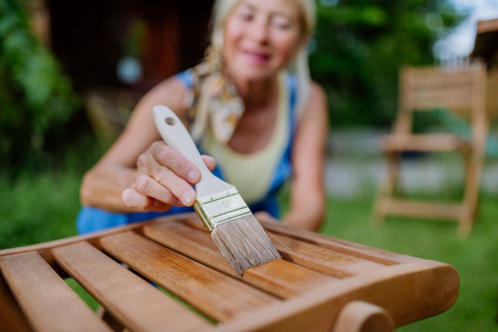 Ältere Frau reinigt und renoviert Gartenmöbel und bereitet den Garten auf den Sommer vor