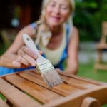 Ältere Frau reinigt und renoviert Gartenmöbel und bereitet den Garten auf den Sommer vor